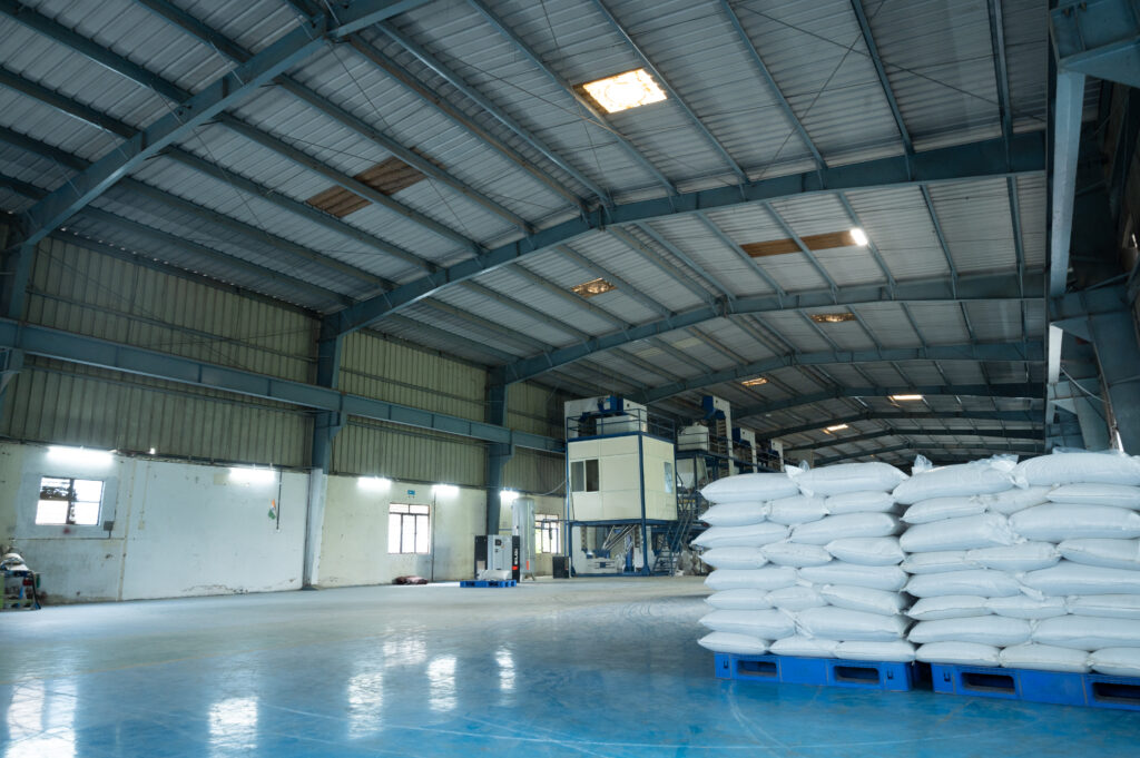 Inside the Quessentials Malur facility — processing tower and stacked finished-product bags